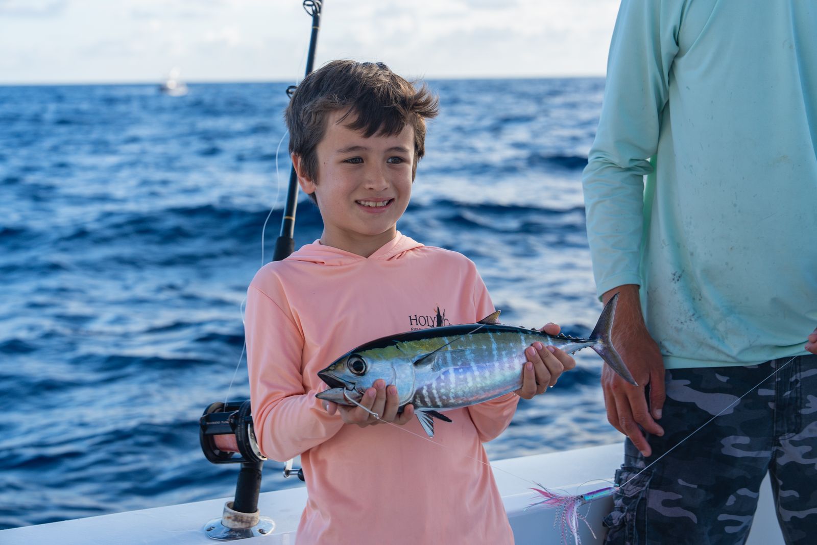 A young angler in pink holding his blackfin tuna aboard a Poppa Wahoo Collective boat