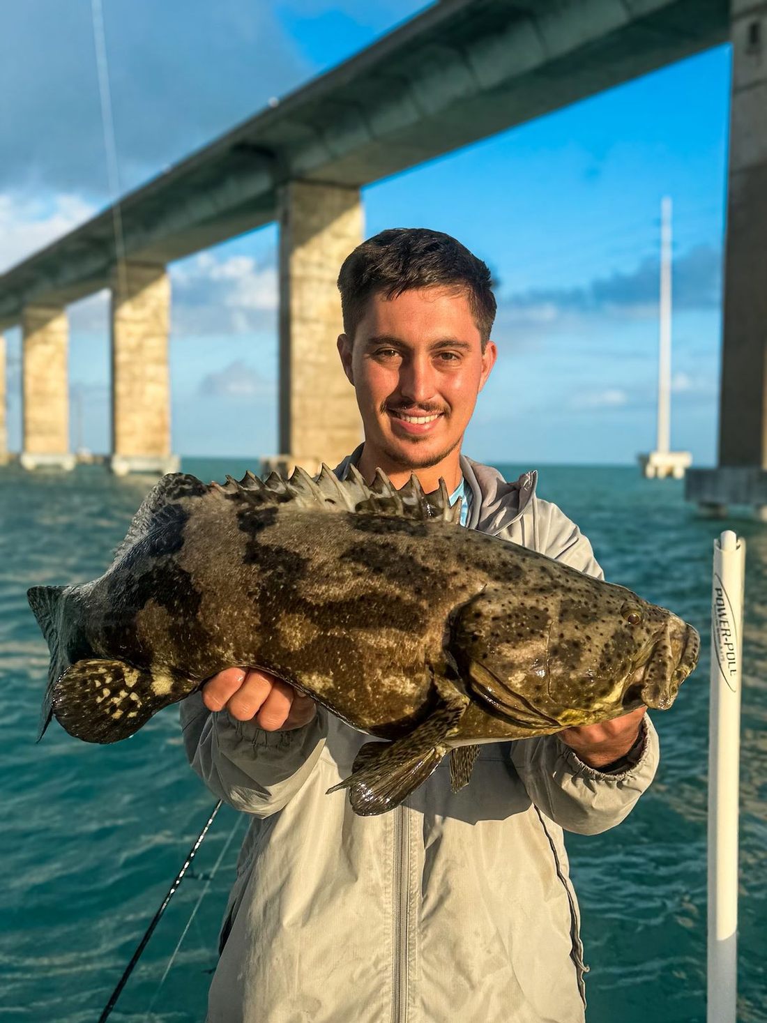 A young angler with a goliath grouper under the bridge